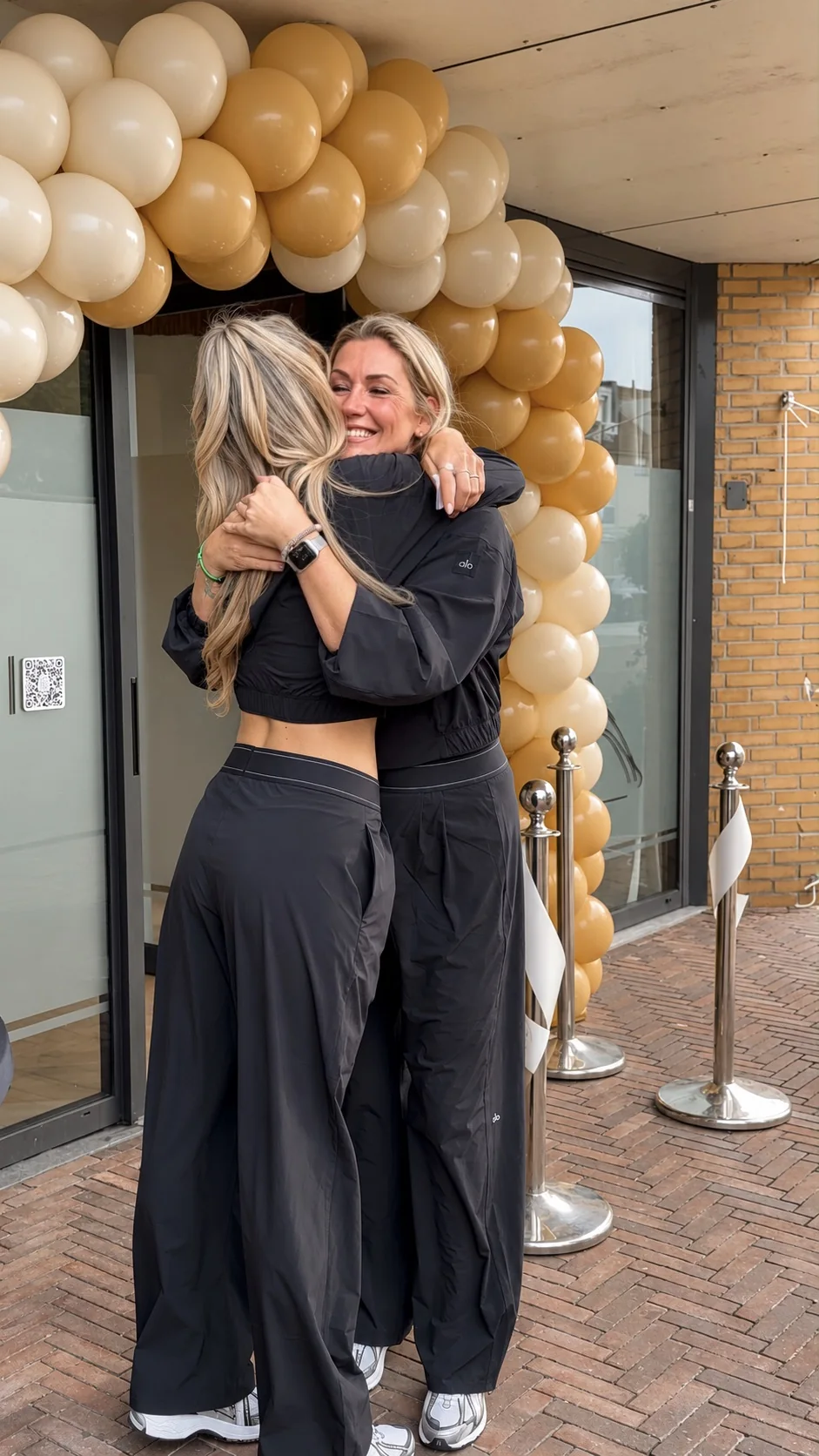 Gladys en Yentel omhelzen elkaar onder de ballonnenboog bij de opening van de nieuwe studio aan het Gruttoplein 4–6 in Diemen-Noord